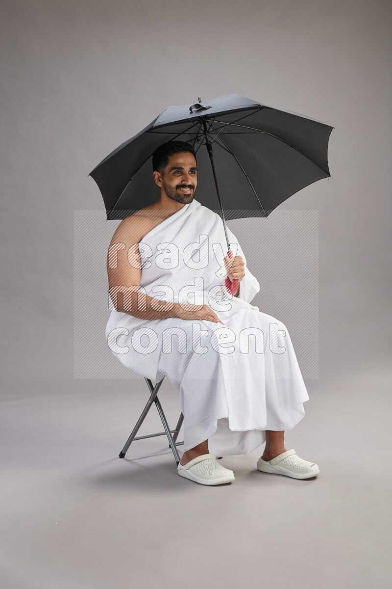 A man wearing Ehram with face mask Standing holding umbrella on gray background