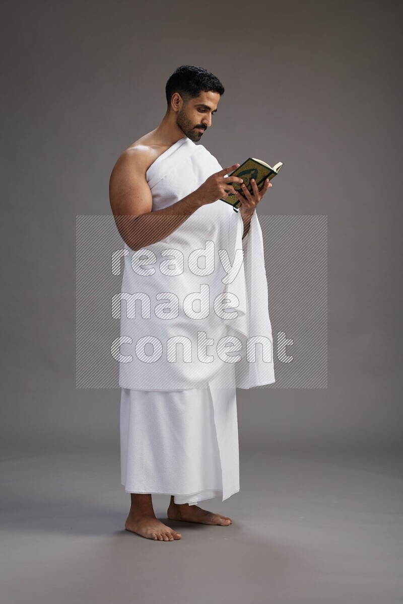 A man wearing Ehram Standing reading quran on gray background
