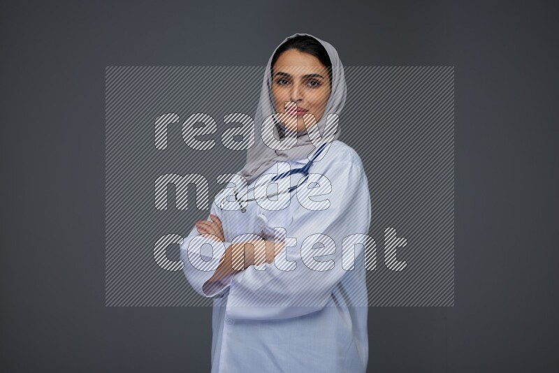 A female doctor wearing a light gray head scarf standing on grey background.