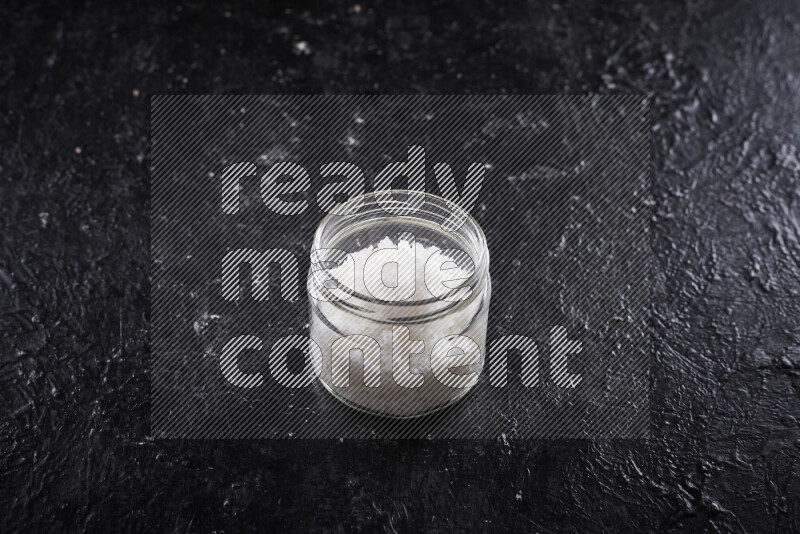 A glass jar full of coarse sea salt crystals on black background