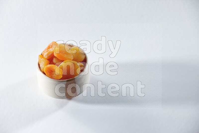 A beige ceramic bowl full of dried apricots on a white background in different angles