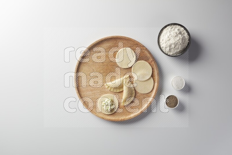 two closed sambosas and one open sambosa filled with cheese while flour, salt, and black pepper aside in a wooden dish on a white background