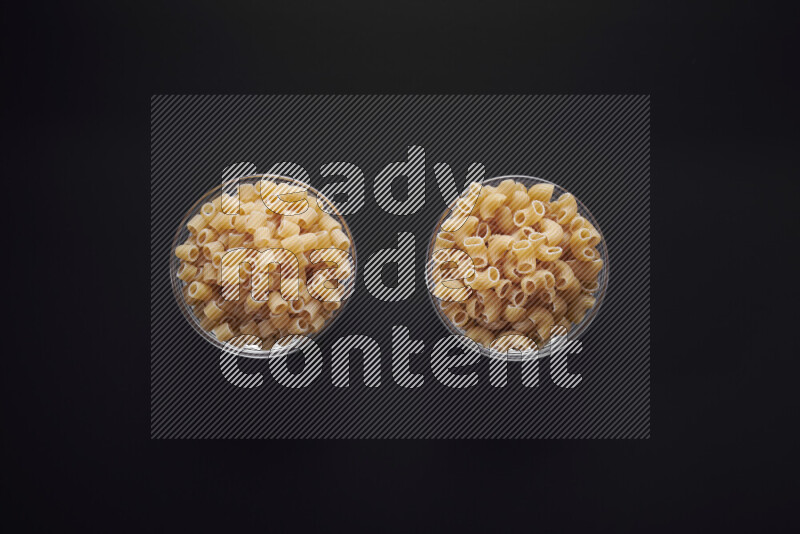 Different pasta types in glass bowls on black background