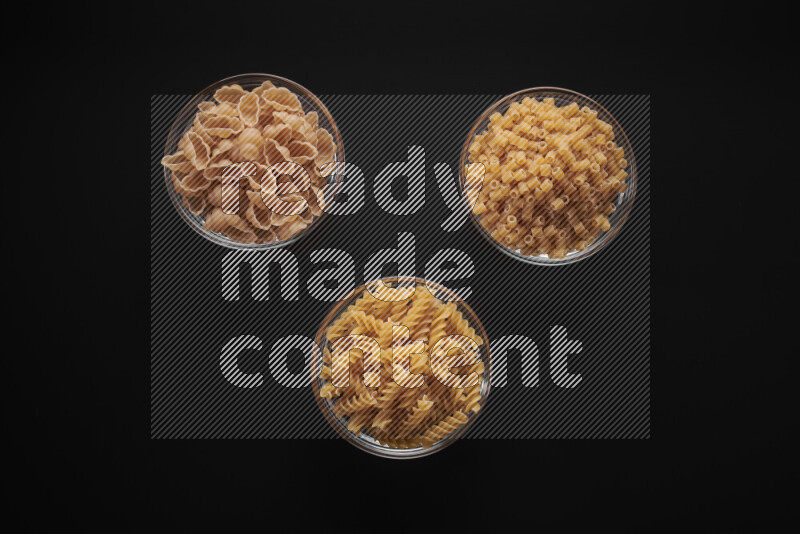 Different pasta types in glass bowls on black background