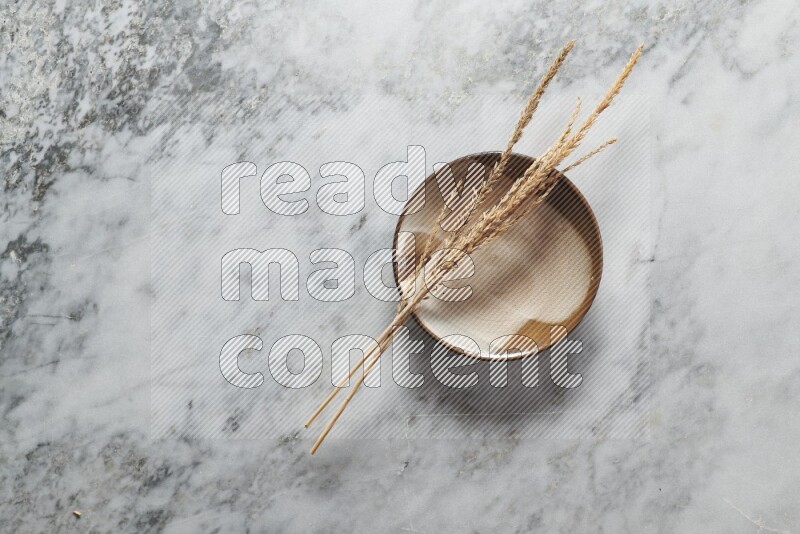 Wheat stalks on multicolored pottery plate on grey marble background