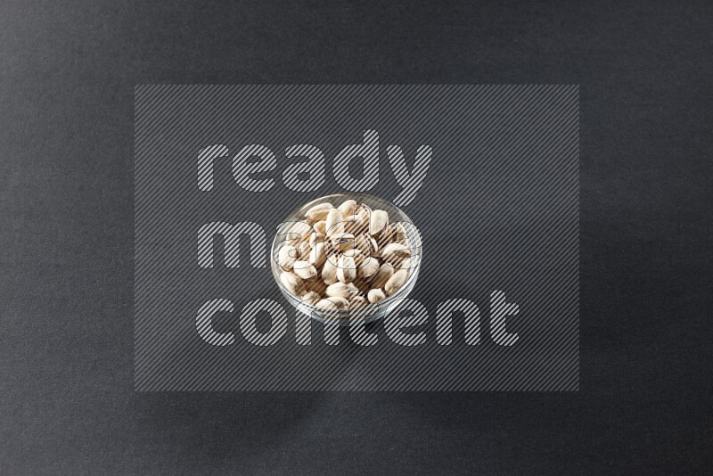 A glass bowl full of pistachios on a black background in different angles