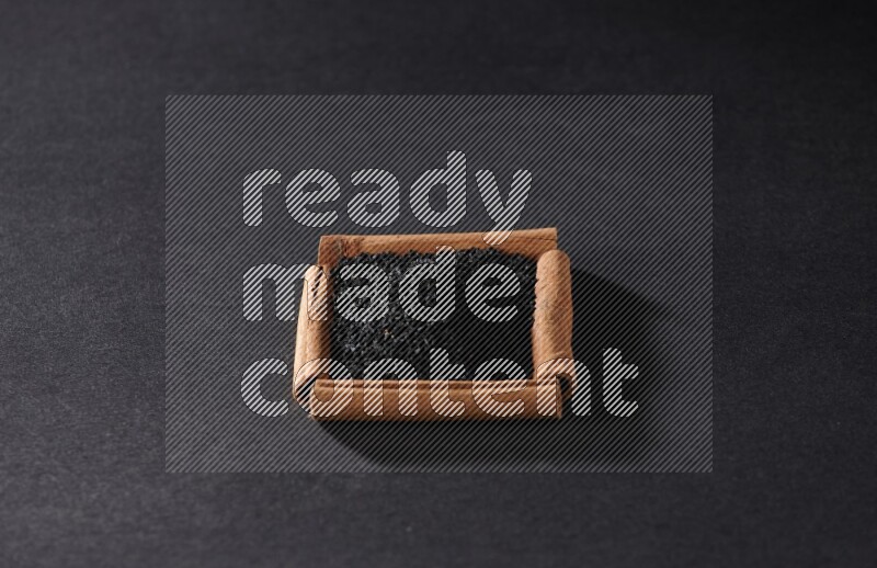 A single square of cinnamon sticks full of black seeds on black flooring
