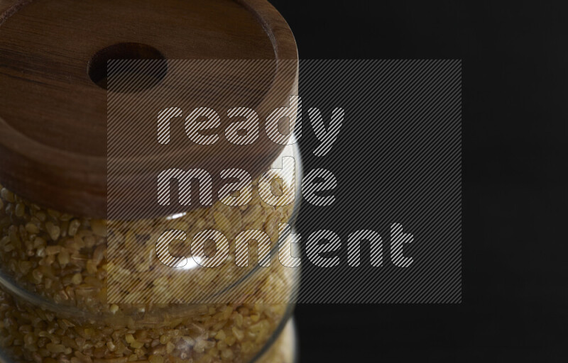 Coarse bulgur in a glass jar on black background
