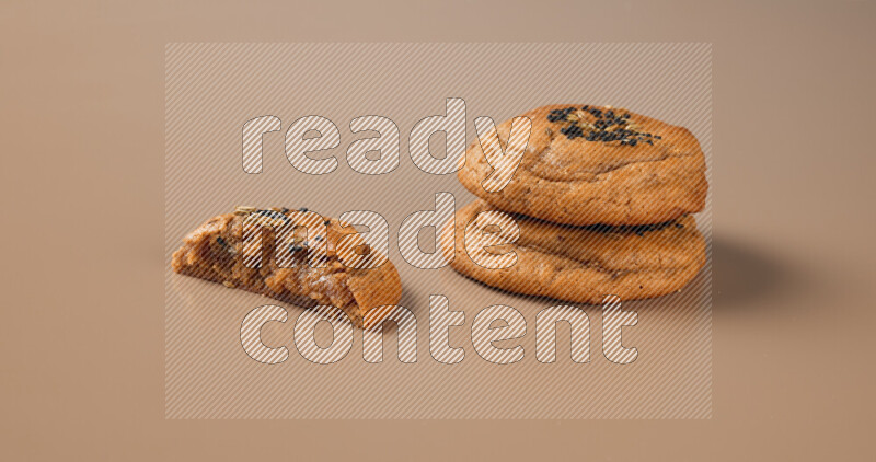 Two Hasawi cookies field of date and decorated by black seed and anise grain with another one cut in half on a brown background