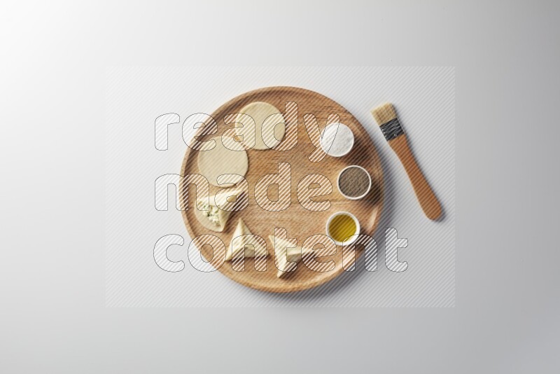 two closed sambosas and one open sambosa filled with cheese while salt, black pepper and oil with oil brush aside in a wooden dish on a white background