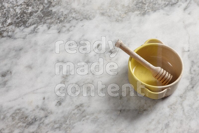 Multicolored pottery bowl with wooden honey dipper in it on grey marble background