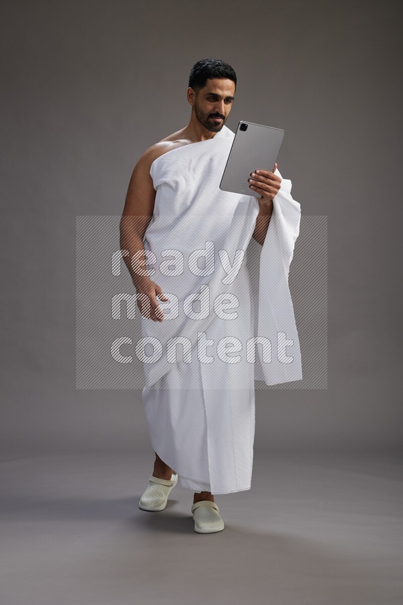 A man wearing Ehram and holding a tablet on gray background