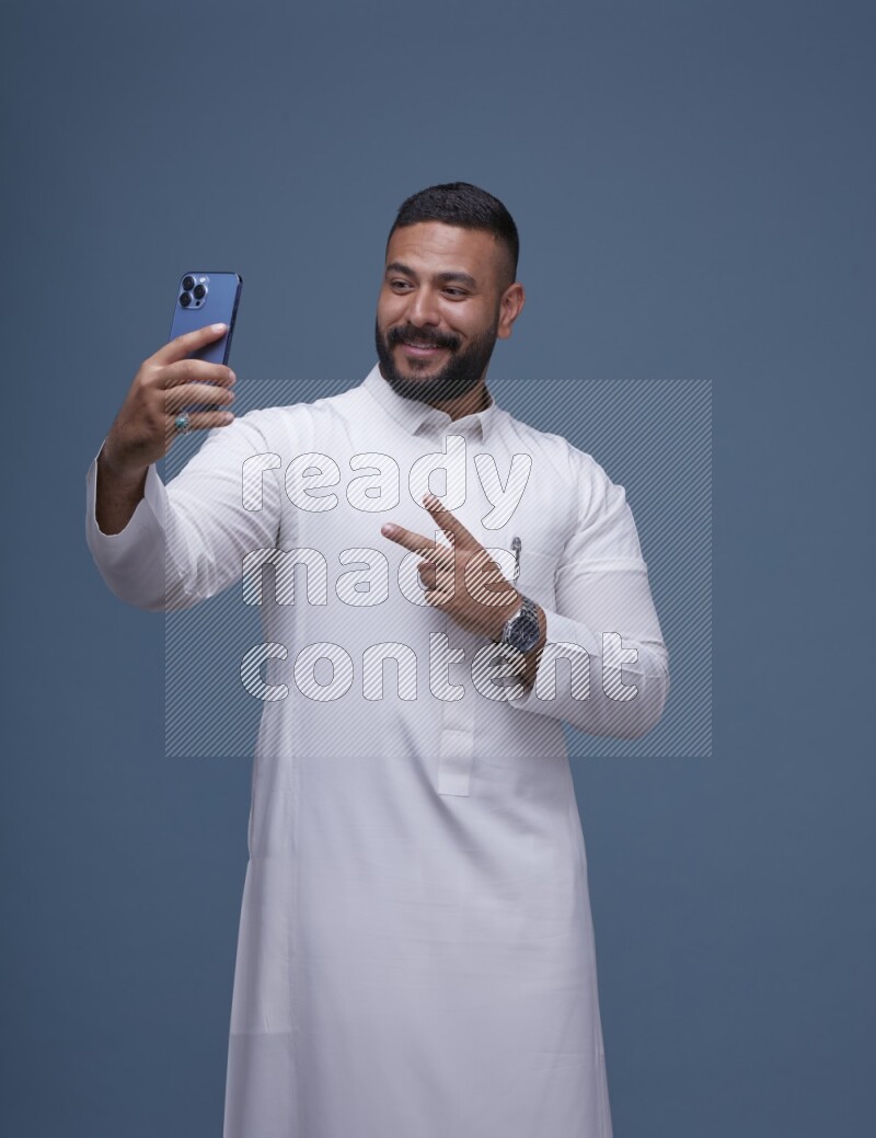 A Saudi man Taking A Selfie on Blue Background wearing Saudi Thob