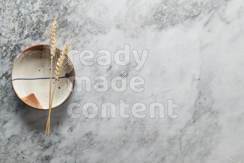 Wheat stalks on multicolored pottery plate on grey marble background