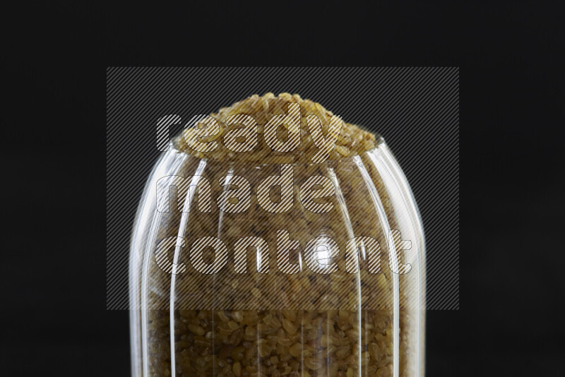 Coarse bulgur in a glass jar on black background