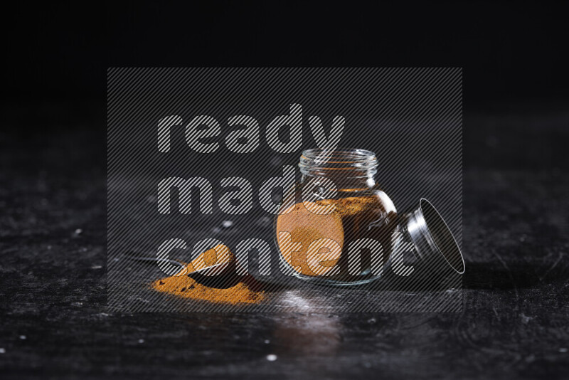 A glass jar full of ground paprika powder on black background