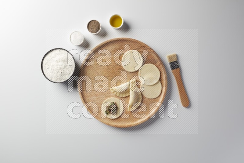 two closed sambosas and one open sambosa filled with meat while flour, salt, black pepper and oil with oil brush aside in a wooden dish on a white background