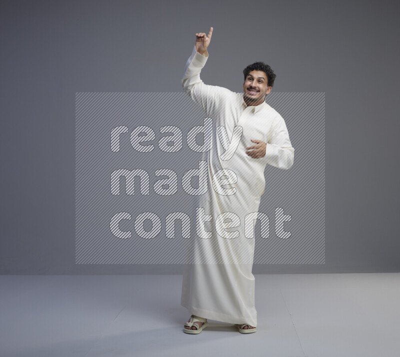 A Saudi man standing wearing thob interacting with the camera on gray background