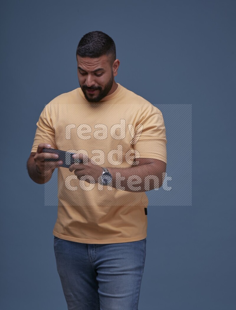A man Playing Games on Smartphone on Blue Background wearing Orange T-shirt