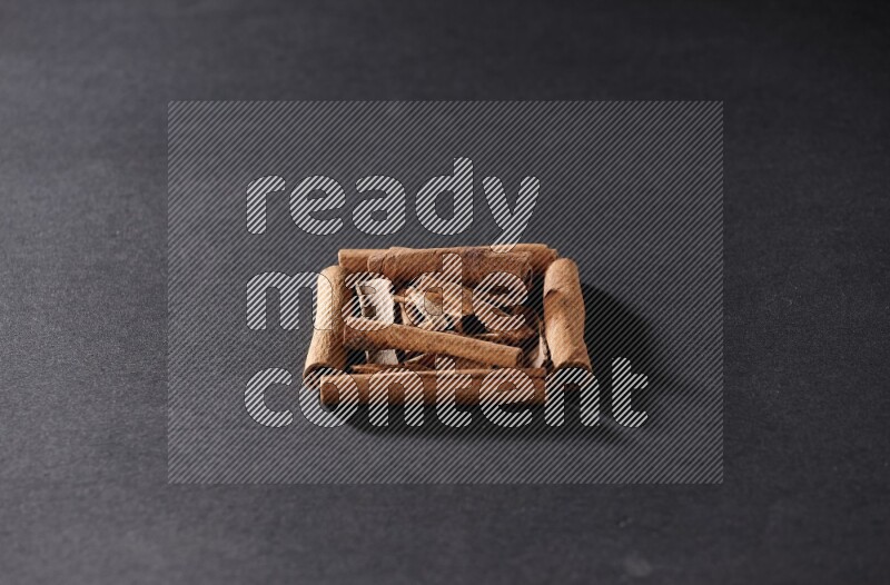 أربعة من أعواد القرفة مكونة شكل مربع بداخلها أعواد قرفة صغيرة علي خلفية سوداء