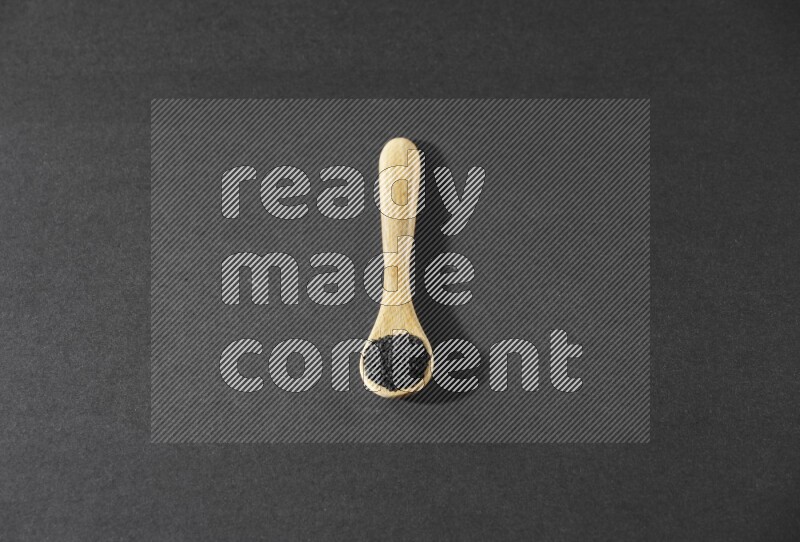 ملعقة خشبية ممتلئة بحبة البركة على أرضية سوداء