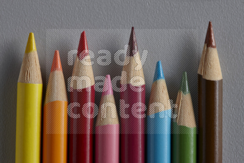 A collection of colored pencils arranged showcasing a gradient of different hues on grey background