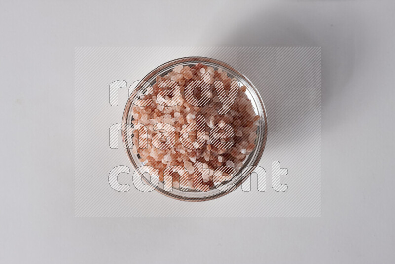A glass bowl full of coarse himalayan salt crystals on white background