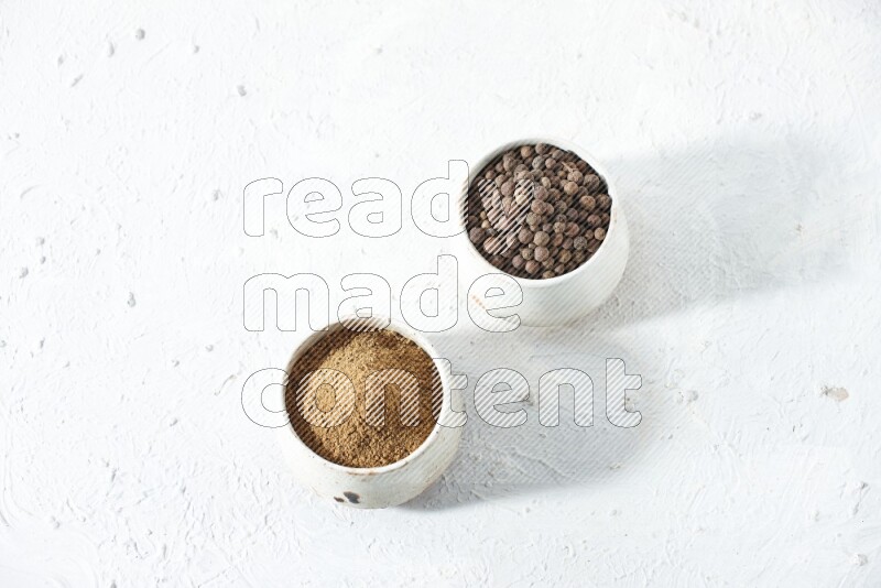 2 beige bowls, one full of allspice powder and the other full of whole balls on a textured white flooring