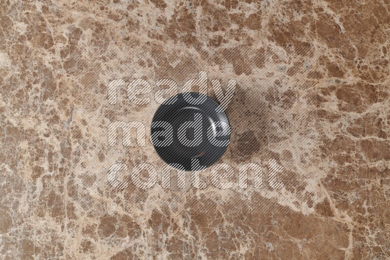 A black ceramic bowl on beige marble background