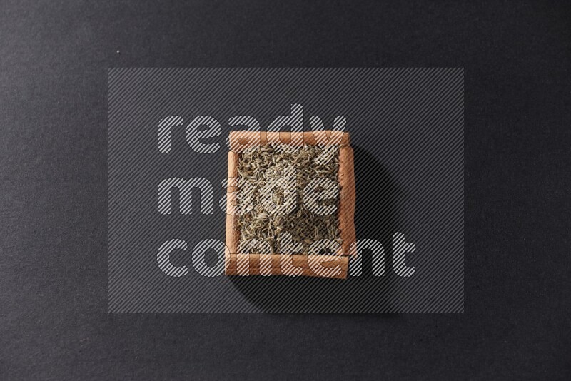A single square of cinnamon sticks full of cumin on black flooring