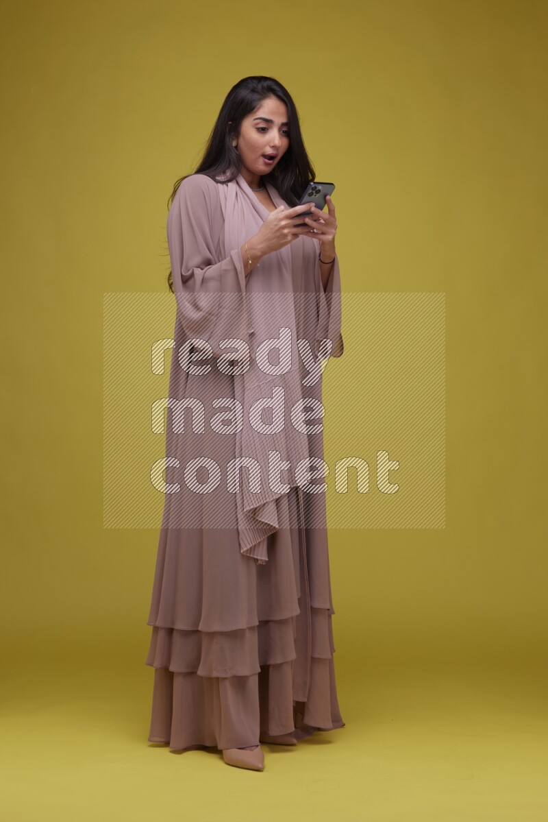 A woman Texting on a Yellow Background wearing Brown Abaya