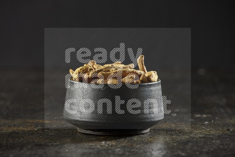 وعاء فخار أسود ممتلئ بأصابع كاملة من الكركم المجفف على خلفية سوداء