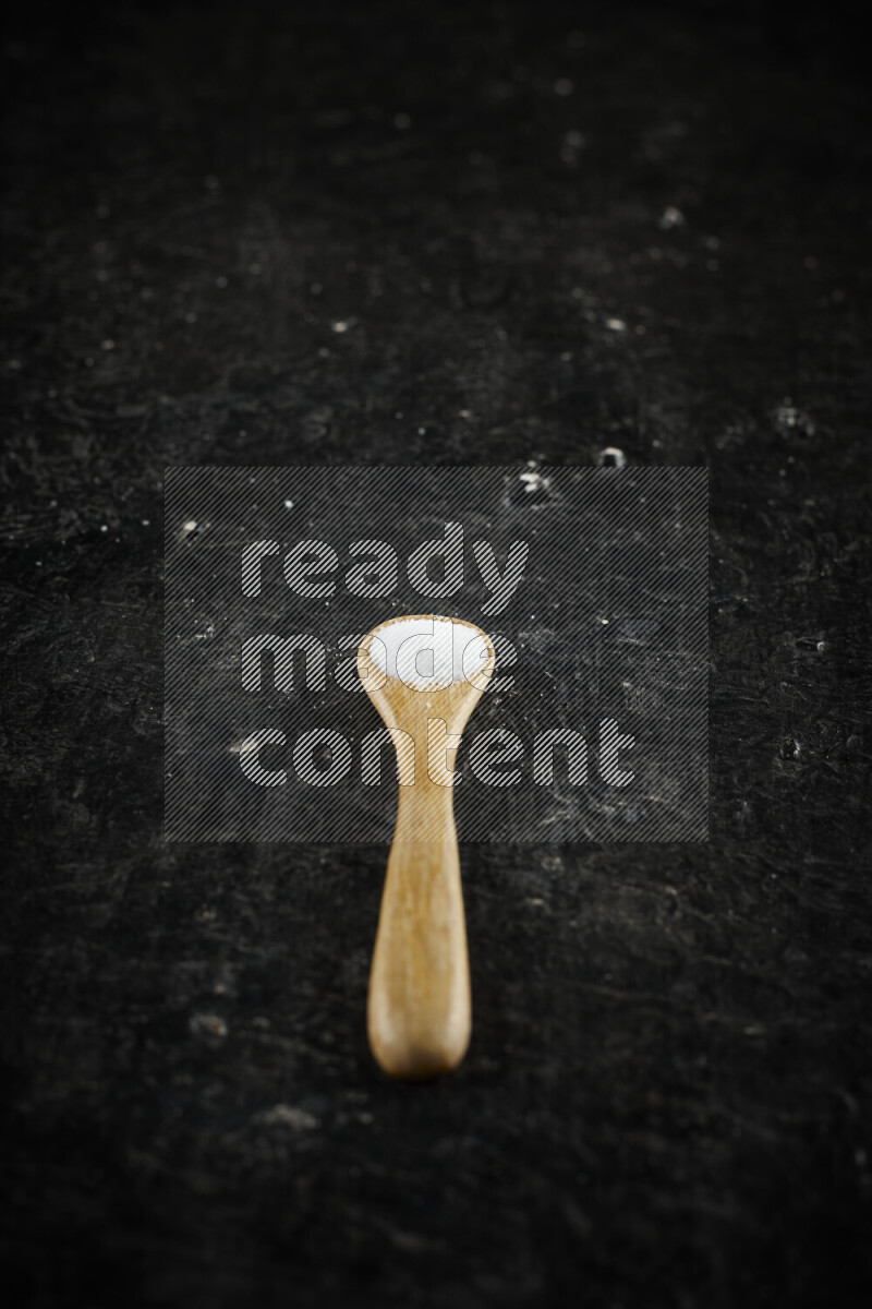 A wooden spoon full of white salt on black background
