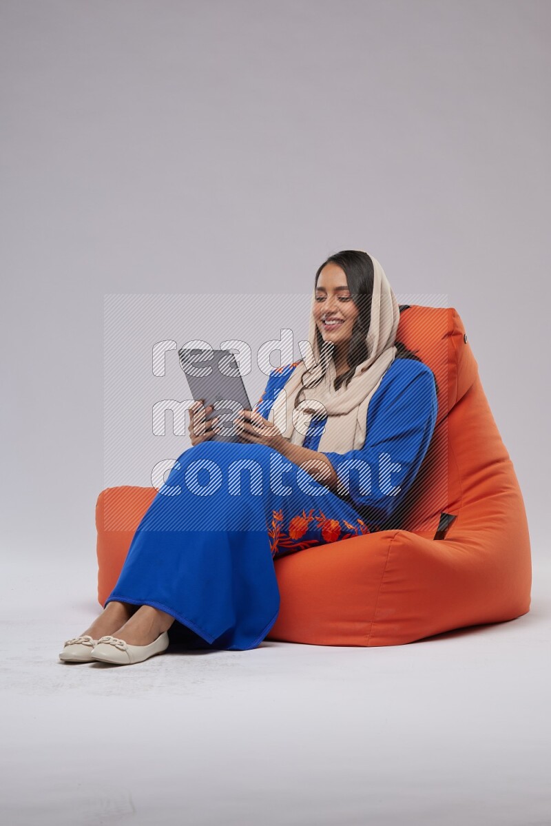 A Saudi woman sitting on an orange beanbag and working on tablet