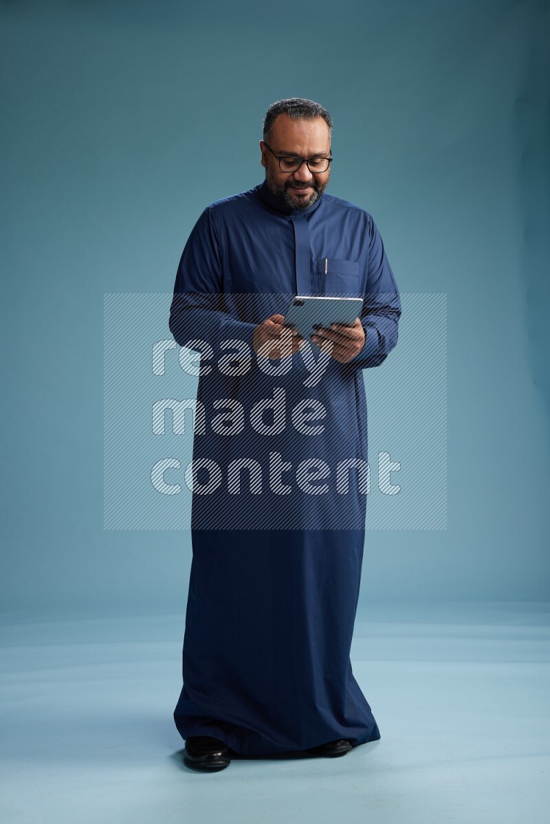 Saudi Man without shimag Standing working on tablet on blue background