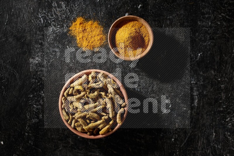 وعاءان خشبيان، أحدهما ممتلئ ببودرة الكركم والآخر بأصابع الكركم المجففة، على خلفية سوداء