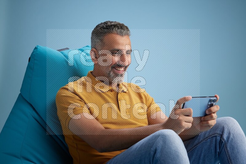 A man sitting on a blue beanbag and playing on phone