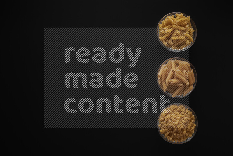 Different pasta types in 3 glass bowls on black background
