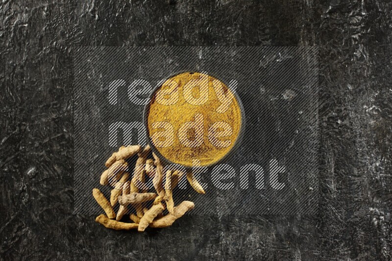 وعاء فخار أسود ممتلئ ببودرة الكركم وأصابع الكركم المجفف بجانبه على خلفية سوداء