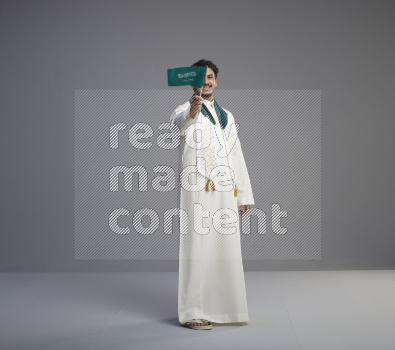 رجل سعودي يرتدي ثوب ابيض ويحمل علم السعودية