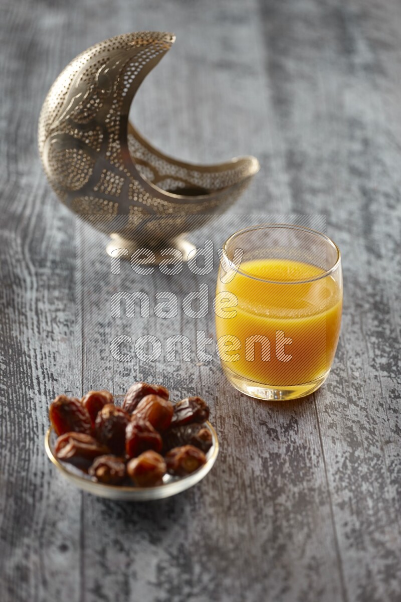 A silver lantern with different drinks, dates, nuts, prayer beads and quran on grey wooden background