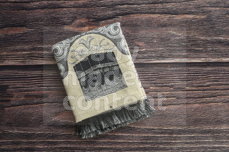 A folded prayer mat with different elements such as quran and prayer beads on brown wooden background