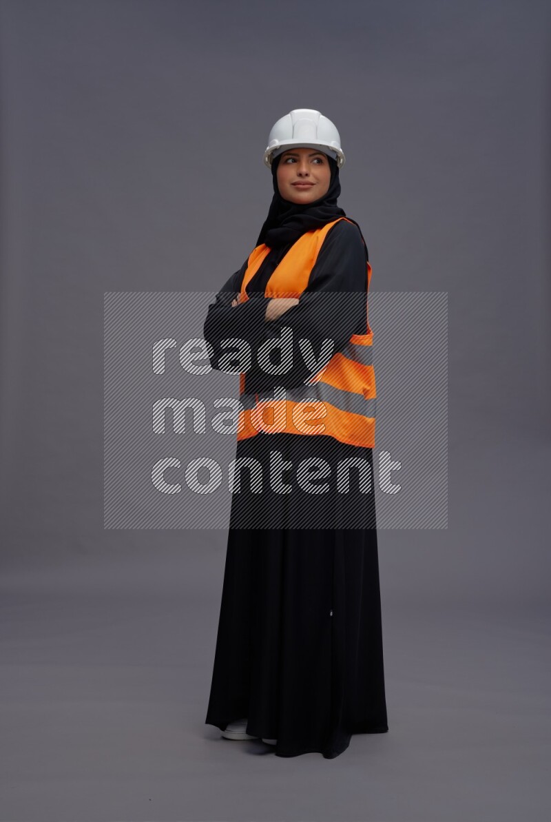 Saudi woman wearing Abaya with engineer vest standing with crossed arms on gray background