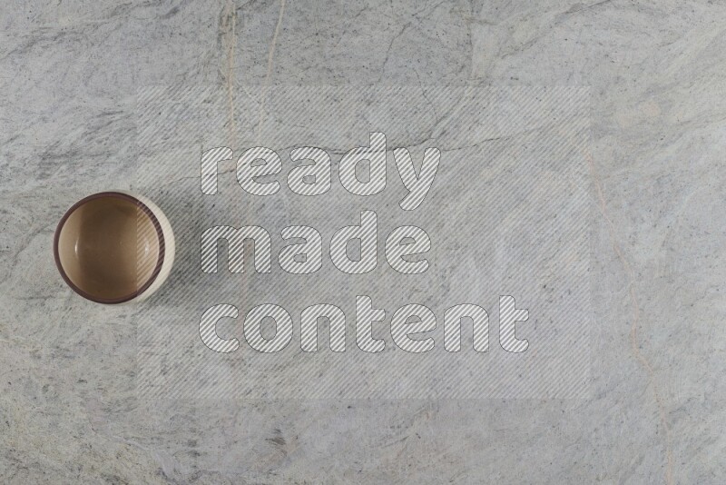 A small beige pottery bowl on grey marble background