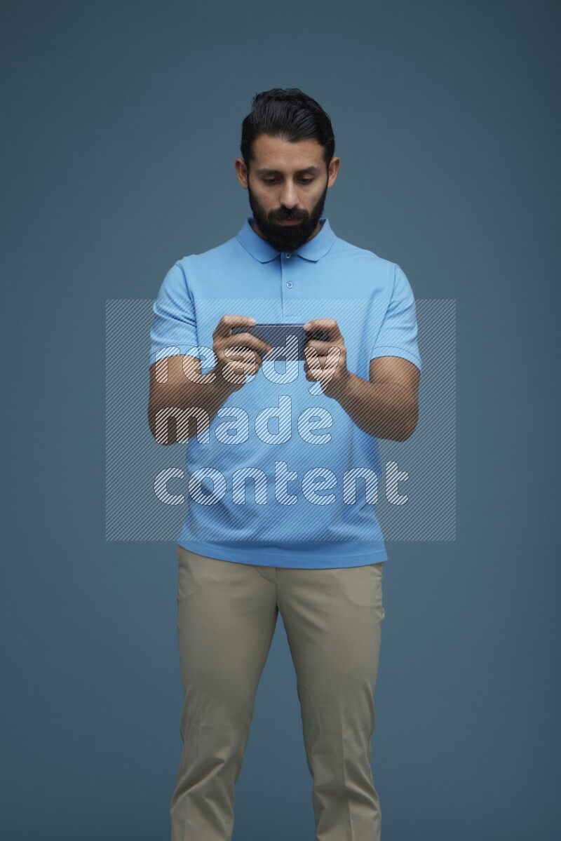 Man playing a game on his phone in a blue background wearing a Blue shirt