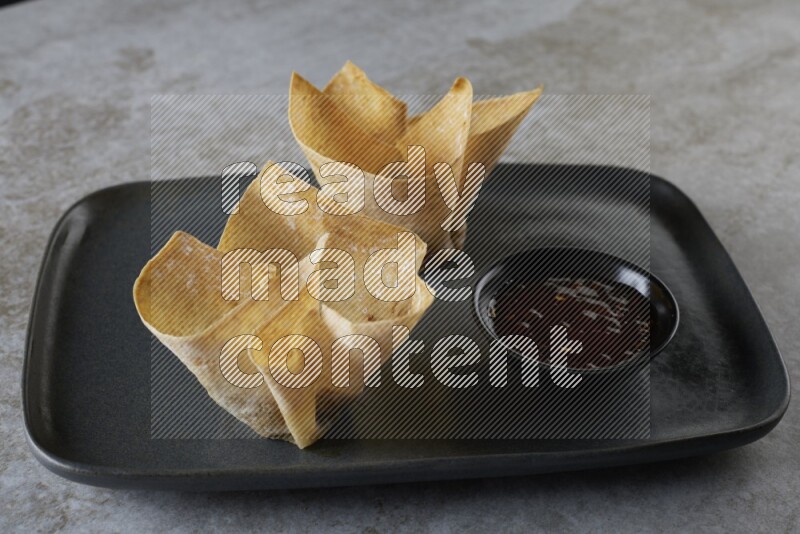 wonton cups with soy sauce ramkin on rectangle dark grey ceramic plate on grey textured counter top