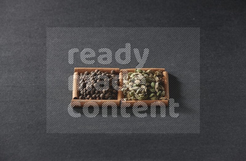 مربعان من أعواد القرفة ممتلئان ببهار الفلفل الحلو وحب الهيل علي خلفية سوداء