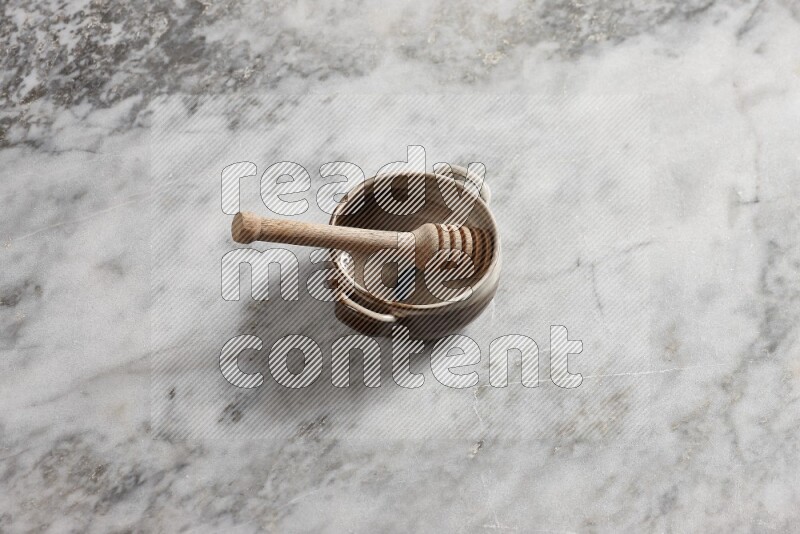 Multicolored pottery bowl with wooden honey dipper in it on grey marble background