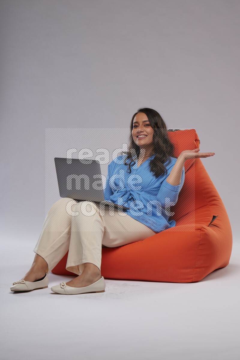 A woman sitting on an orange beanbag and working on laptop
