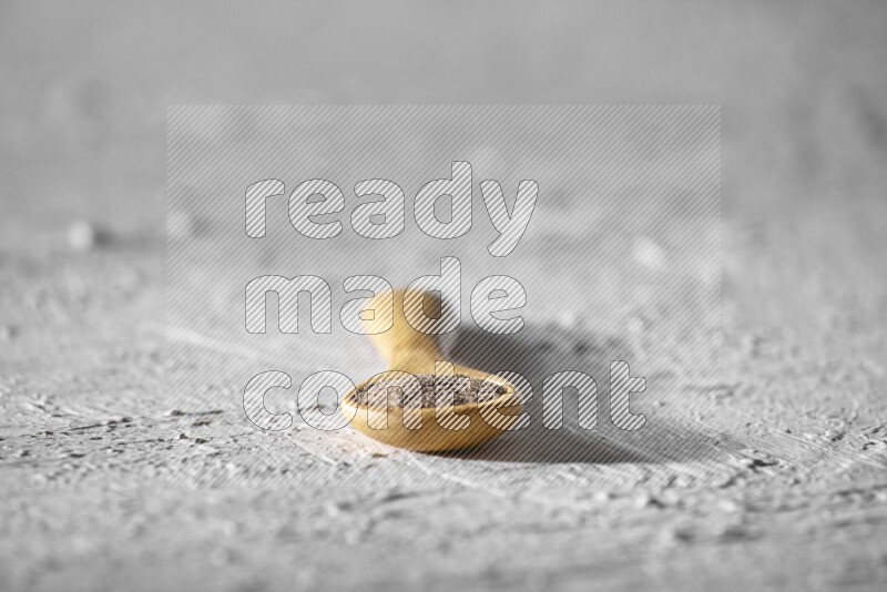 A wooden spoon full of black pepper powder on a textured white flooring